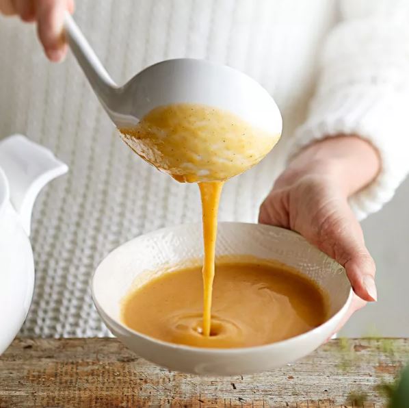 Soup being ladled into a white bowl 