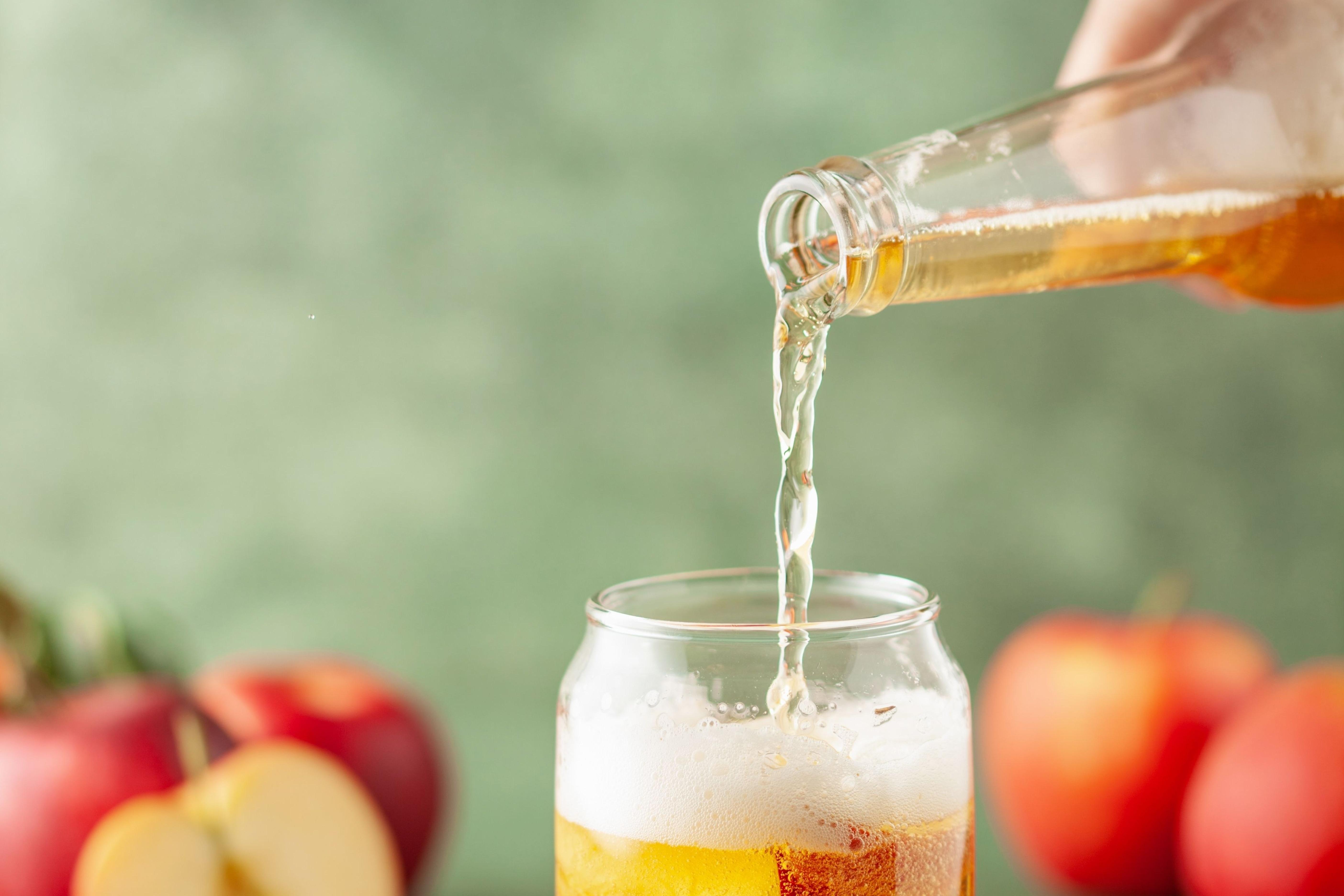 hard cider being poured into glass in front of apples
