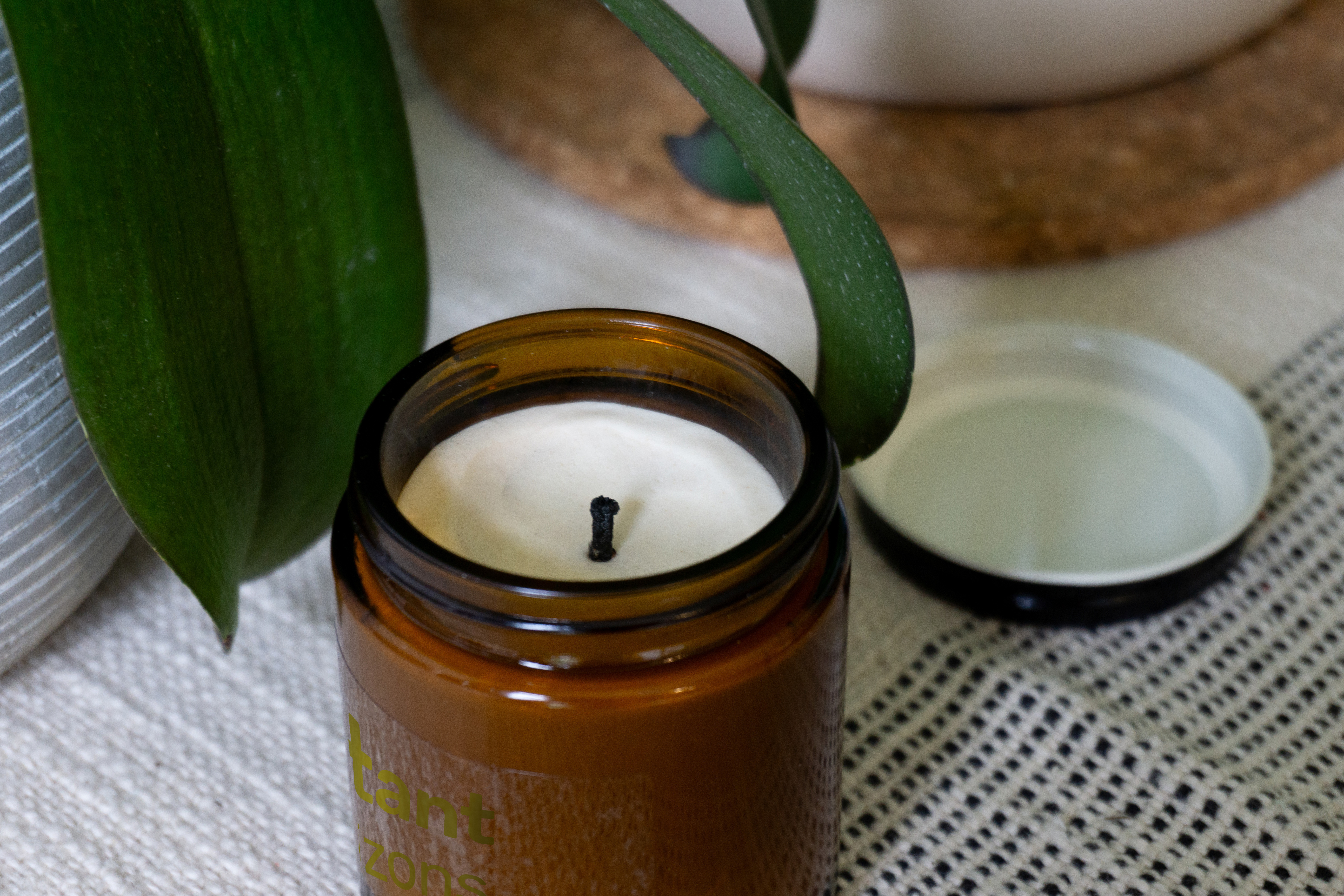 An amber glass candle jar set on a shelf with a book and a plant