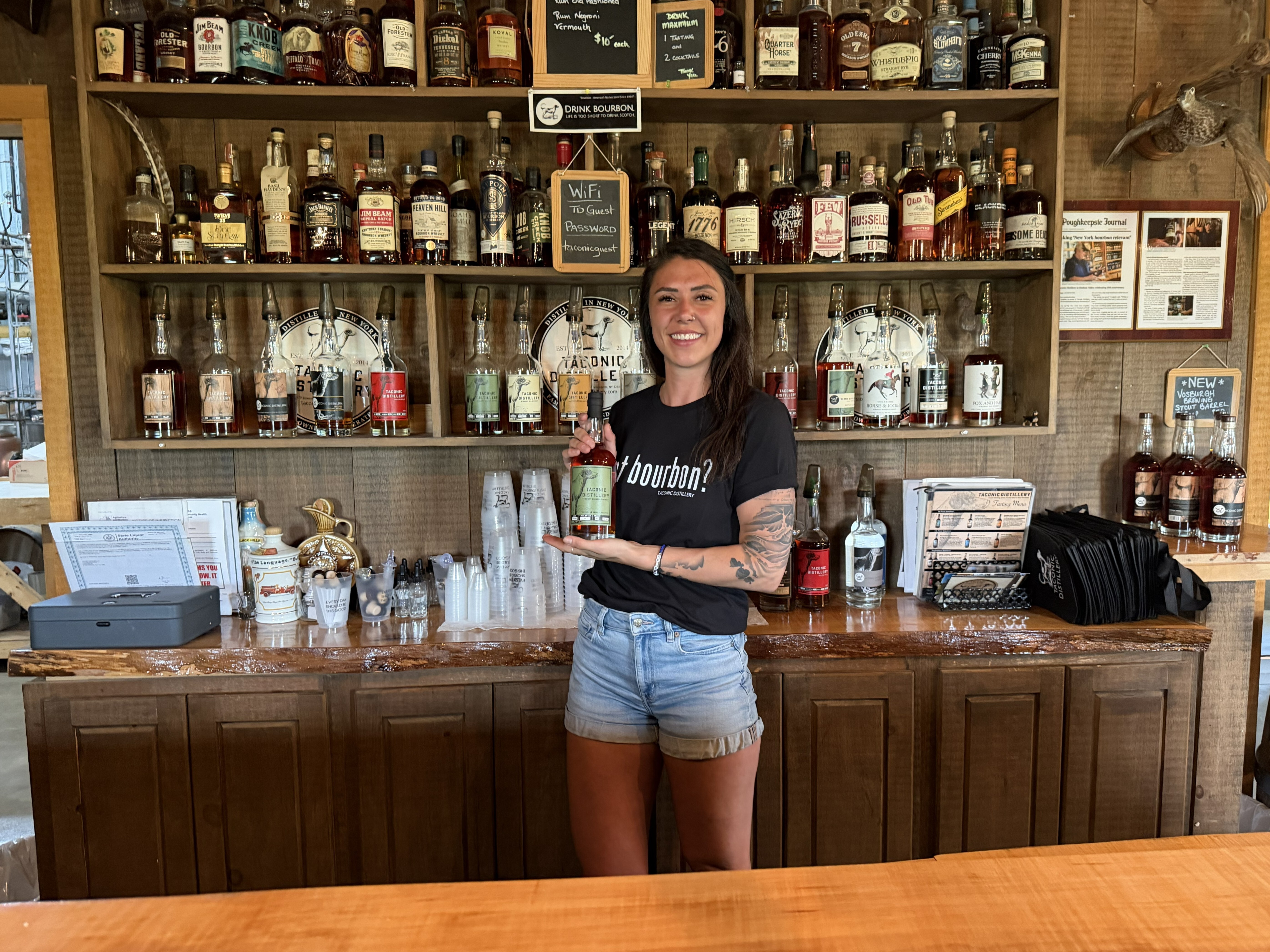 Gabby holding a bottle of liquor behind a wooden bar
